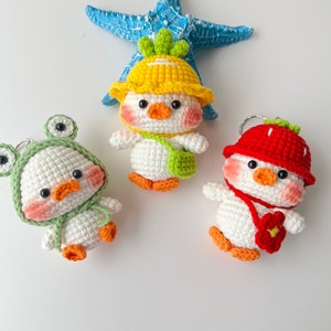 May include: Three crocheted stuffed animal keychains. One is a yellow chick with a green hat, one is a green frog with a white hat, and one is a red strawberry with a white hat.
