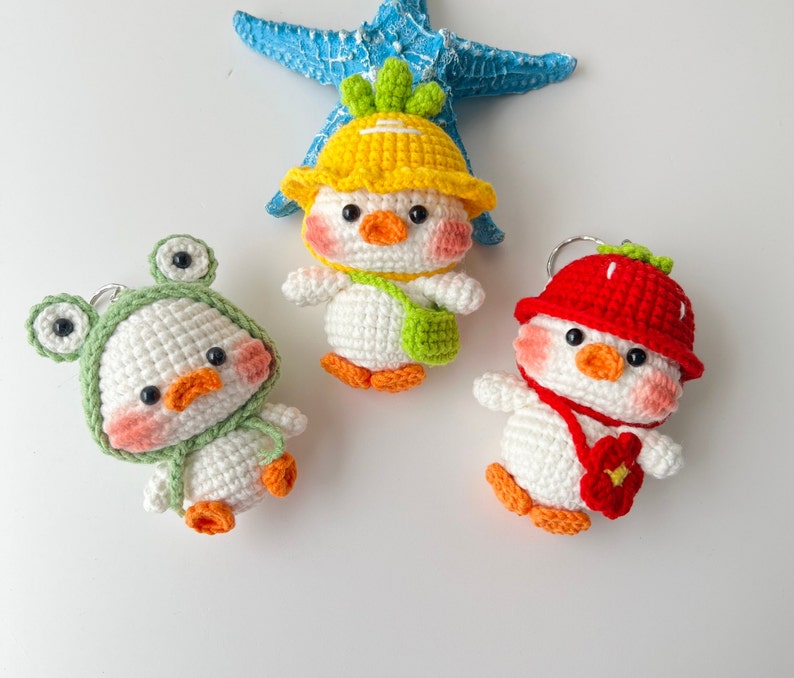 May include: Three crocheted stuffed animal keychains. One is a yellow chick with a green hat, one is a green frog with a white hat, and one is a red strawberry with a white hat.