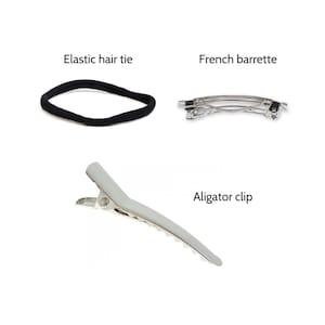 K&ouml;nnte beinhalten: Drei Haarschmuckst&uuml;cke: ein schwarzes Gummiband, eine silberne Alligator-Klammer und eine silberne franz&ouml;sische Barrette.