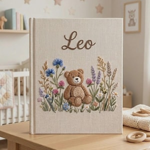 Puede incluir: Un &aacute;lbum de recuerdos para beb&eacute;s con cubierta de lino beige con el nombre "Leo" bordado en escritura marr&oacute;n. La portada presenta un oso de peluche bordado rodeado de flores coloridas. Un recuerdo encantador para beb&eacute;s.