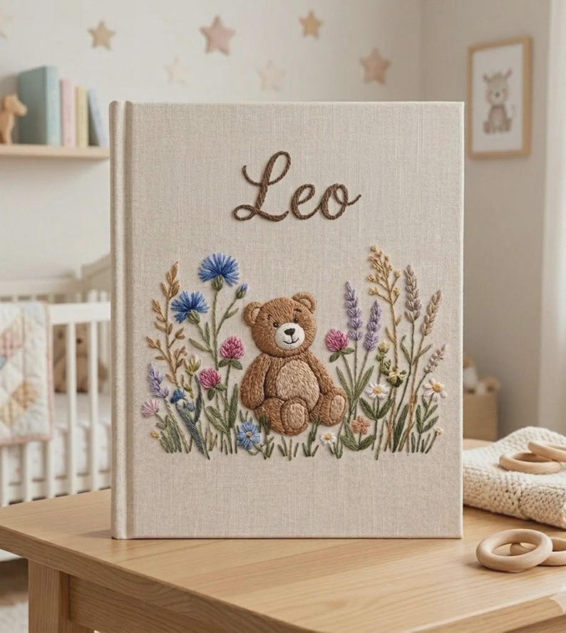 Puede incluir: Un &aacute;lbum de recuerdos para beb&eacute;s con cubierta de lino beige con el nombre "Leo" bordado en escritura marr&oacute;n. La portada presenta un oso de peluche bordado rodeado de flores coloridas. Un recuerdo encantador para beb&eacute;s.