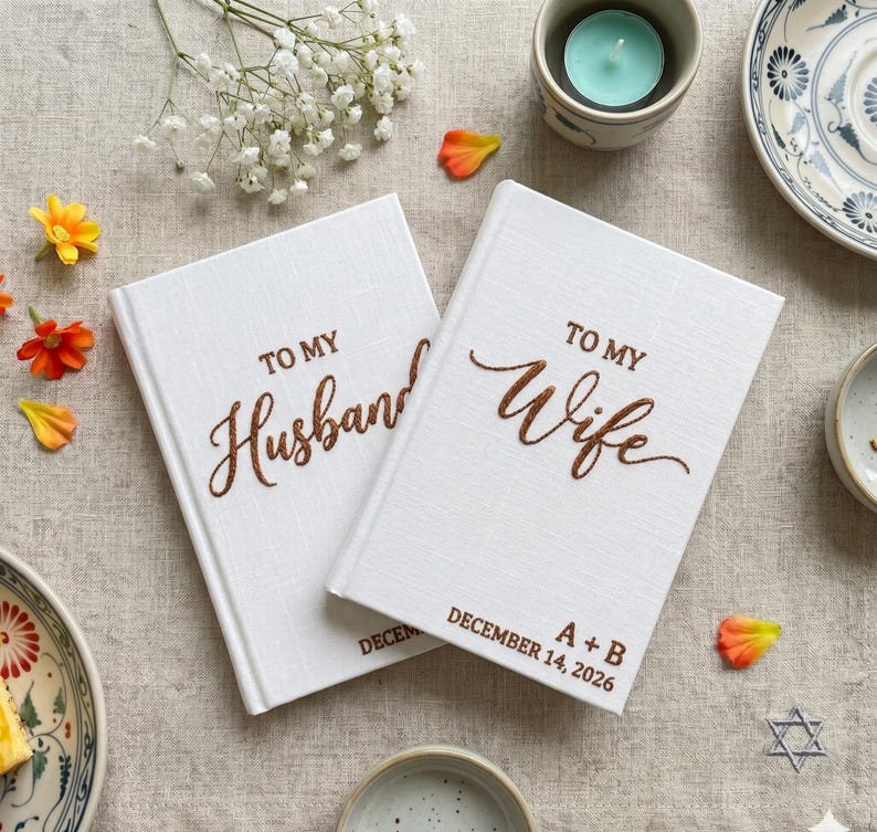 Pode incluir: Dois livros de capa dura branca com superf&iacute;cies texturizadas. Um livro apresenta o texto castanho TO MY Husband, e o outro apresenta TO MY Wife, A + B, e DECEMBER 14, 2026. Os livros est&atilde;o posicionados lado a lado numa superf&iacute;cie de tecido.