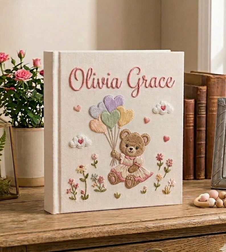 Puede incluir: Libro de recuerdos para beb&eacute;s de color crema con detalles bordados. Presenta el nombre "Olivia Grace" en escritura rosa. Un osito de peluche sosteniendo globos pastel est&aacute; centrado, rodeado de flores y corazones.