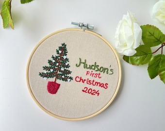 Può includere: Addobbo natalizio ricamato con un albero di Natale verde e il testo "Hudson's First Christmas 2024" in filo rosso e verde.