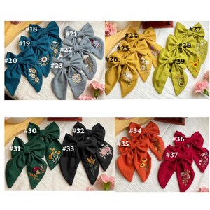 K&ouml;nnte beinhalten: Ein Set mit 37 handgefertigten Stoffhaarb&auml;ndern mit gestickten Blumenmustern. Die Schleifen sind in verschiedenen Farben, darunter T&uuml;rkis, Gelb, Gr&uuml;n, Schwarz, Rot und Orange.