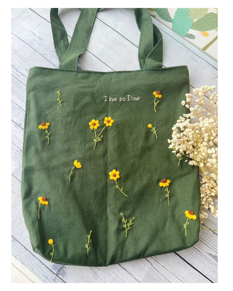 May include: A dark green canvas tote bag with embroidered yellow flowers and the text "I live so I love".