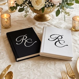 Pode incluir: Dois livros de capa dura com revestimento em tecido, um preto com letras de monograma RC bordadas em branco e um branco com letras de monograma RC bordadas em preto. Os livros s&atilde;o retangulares com uma lombada limpa e acabamento texturizado.