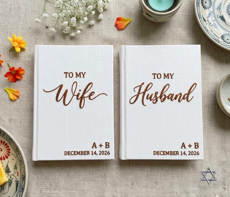 Pode incluir: Dois livros de capa dura brancos com texto castanho. O livro da esquerda diz TO MY Wife A + B DECEMBER 14, 2026. O livro da direita diz TO MY Husband A + B DECEMBER 14, 2026. As capas t&ecirc;m um acabamento em tecido texturizado.