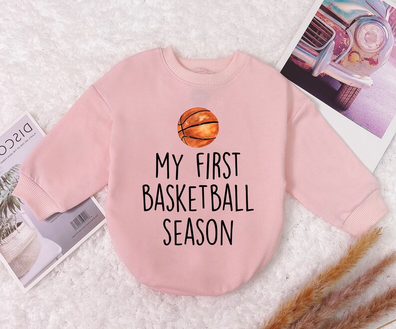 May include: Pink long-sleeved sweatshirt with a basketball graphic and the text "My First Basketball Season".