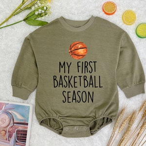 May include: A green long-sleeved baby onesie with a basketball graphic and the text "My First Basketball Season".
