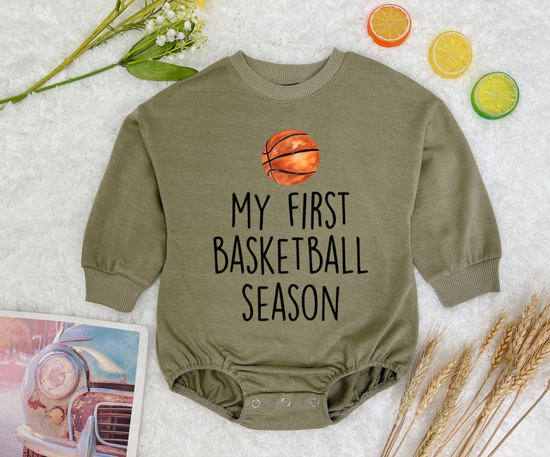 May include: A green long-sleeved baby onesie with a basketball graphic and the text "My First Basketball Season".
