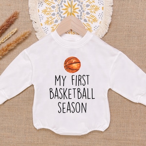 May include: White long-sleeved onesie with a basketball graphic and the text "My First Basketball Season!"