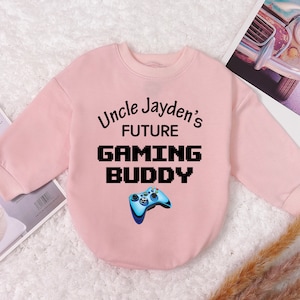 May include: Pink long-sleeved sweatshirt with the text "Uncle Jayden's Future Gaming Buddy" in black pixelated font. A blue video game controller graphic is below the text.