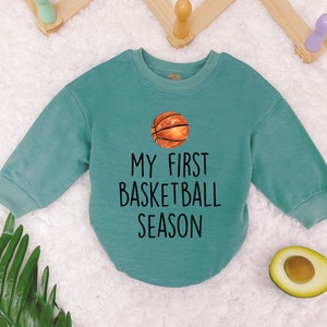May include: A teal blue long-sleeved sweatshirt with the text "My First Basketball Season" and a cartoon basketball graphic.