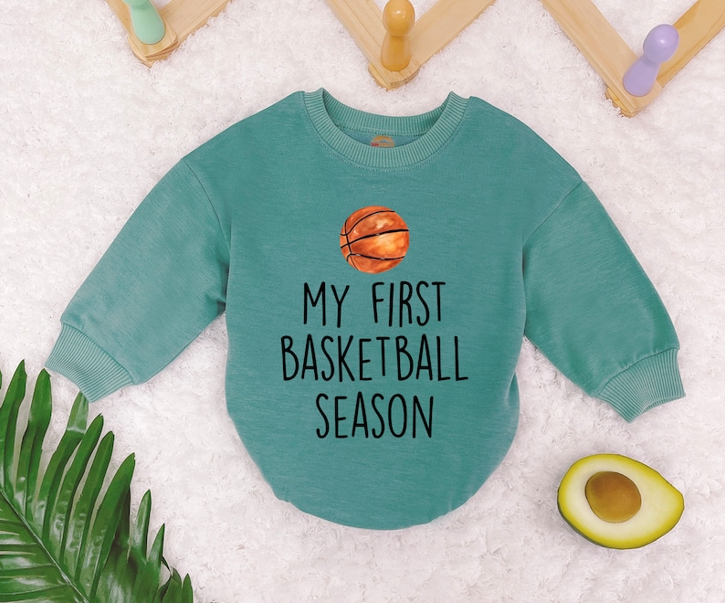 May include: A teal blue long-sleeved sweatshirt with the text "My First Basketball Season" and a cartoon basketball graphic.