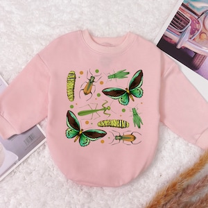 May include: A pink long-sleeved sweatshirt with a graphic print of butterflies, caterpillars, and insects in shades of green, yellow, and brown.