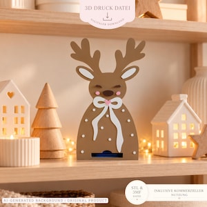 Può includere: Un file di stampa 3D a forma di renna marrone con un fiocco bianco e un cuore rosa, occhi chiusi e pois bianchi. Il design presenta una fessura rettangolare alla base. Il testo include 3D DRUCK DATEI, DIGITALER DOWNLOAD, STL & 3MF DATEI e INKLUSIVE KOMMERZIELLER NUTZUNG.