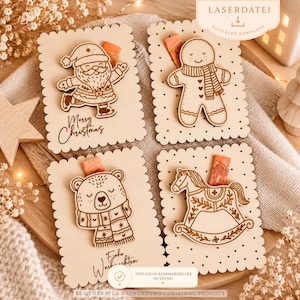 Puede incluir: Cuatro tarjetas rectangulares de madera con bordes festoneados, cada una con un diseño navideño grabado con láser: un Santa Claus con el texto Merry Christmas, un hombre de jengibre, un oso con bufanda y el texto Frohe Weihnachten, y un caballito balancín.