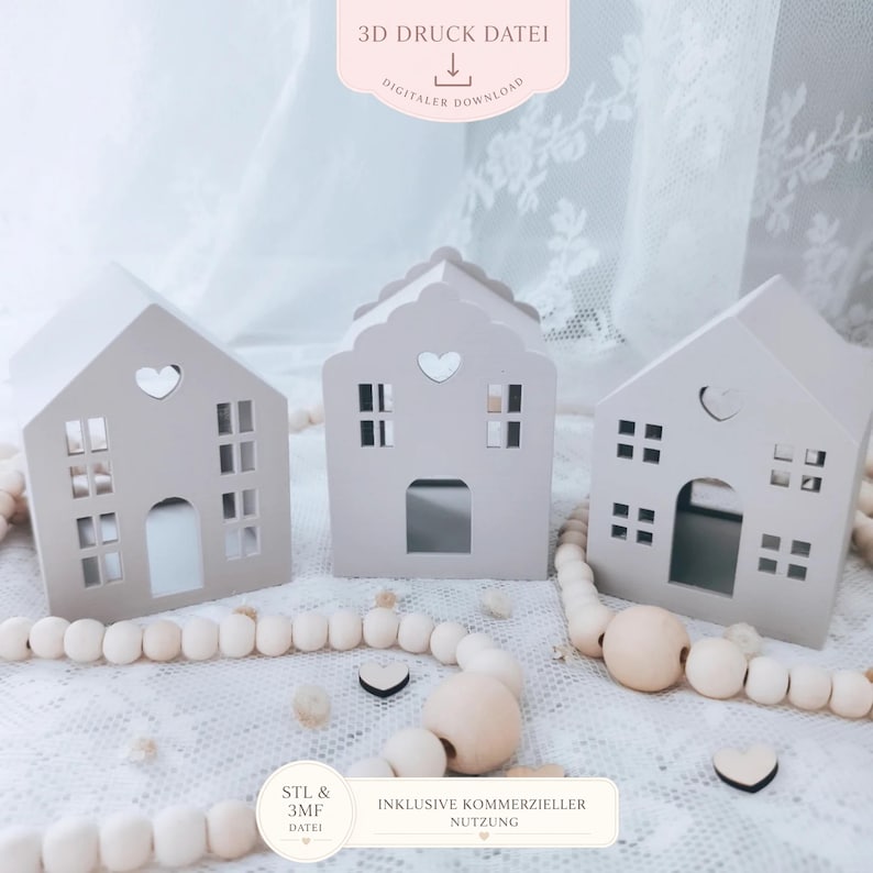 May include: Three light grey miniature house decorations with heart-shaped cutouts and window details. The houses are arranged on a white lace surface, accompanied by wooden beads and small heart-shaped accents. The image includes text that reads "3D Druck Datei" and "Digitaler Download".