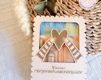 May include: A wooden cutout of a heart being held by two hands with the text "kleiner Herzenswunsch erfüller" below. The cutout is designed to hold money as a gift.