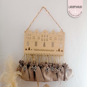 Puede incluir: Un calendario de adviento de madera con forma de casa con 24 pequeñas bolsas de arpillera colgando. Las bolsas están numeradas del 1 al 24. La casa tiene un diseño recortado y las palabras "Adventskalender" están escritas en la parte delantera.
