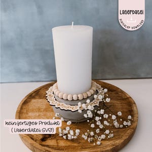May include: A white candle sits on a wooden base with a decorative wooden ring and wooden beads. The base is on a wooden tray. The text "kein fertiges Produkt (LaserdDatei SVG)" is visible in the image.
