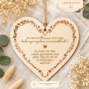 May include: A heart-shaped wooden plaque with a floral border and a jute string for hanging. The plaque features engraved text in German, including the words "Mama" and "Leben". The design is a light brown color.
