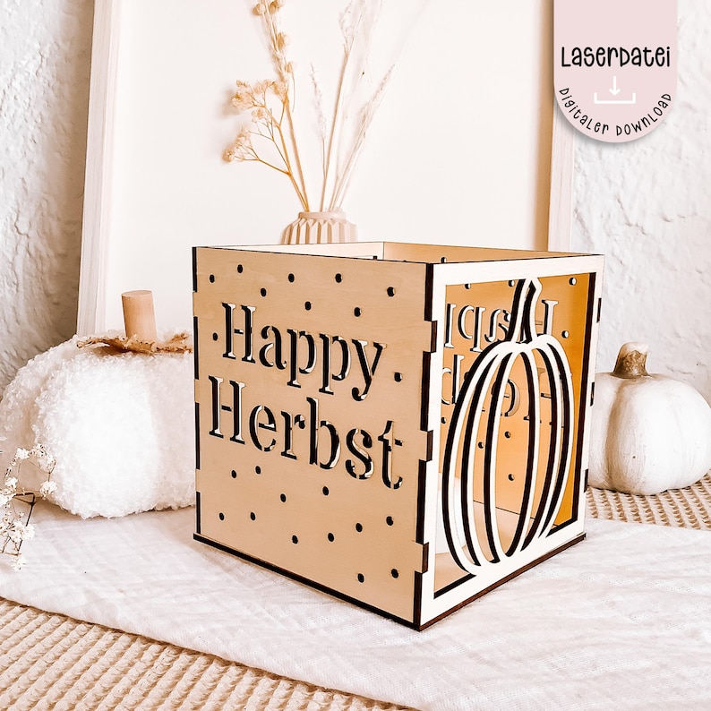 K&ouml;nnte beinhalten: Eine Holzkiste mit den ausgeschnittenen Worten "Happy Herbst" und einem K&uuml;rbismotiv. Die Kiste ist von dekorativen K&uuml;rbissen und Trockenblumen umgeben, was ein Herbstthema erzeugt. Die Kiste ist aus hellem Holz gefertigt.
