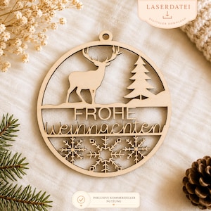 Pode incluir: Um enfeite de Natal de madeira cortado a laser com uma rena, um pinheiro e flocos de neve dentro de uma moldura circular. A frase alemã "Frohe Weihnachten" é exibida. O enfeite tem um pequeno orifício para pendurar.