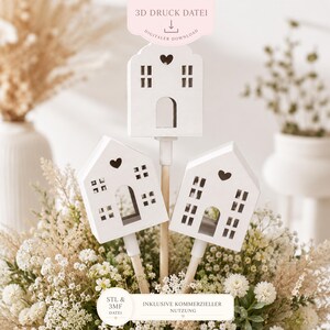 May include: Three white, house-shaped decorations with heart and square window cutouts, mounted on wooden sticks, are arranged in a floral display. The image includes text that reads "3D Druck Datei" and "Digitaler Download".