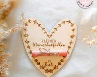 May include: A wooden heart-shaped plaque with a scroll tied with twine that reads "KLEINER WUNSCHERFÜLLER FÜR DICH". The plaque is decorated with a floral design.