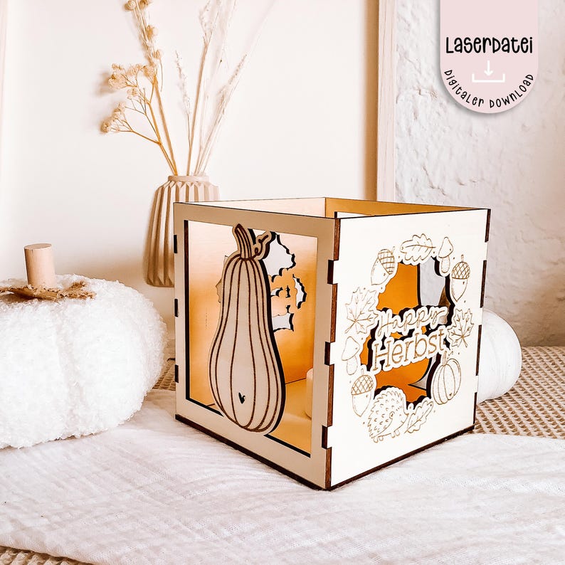 K&ouml;nnte beinhalten: Eine w&uuml;rfelf&ouml;rmige Holzlaterne mit lasergeschnittenen Herbstmotiven. Die Laterne zeigt einen K&uuml;rbis und die Worte "Happy Herbst". Das Design umfasst Bl&auml;tter, Eicheln und einen Igel. Der Text "Laserdatei digitaler download" ist ebenfalls sichtbar.
