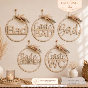 Op de afbeelding: Vijf ronde houten wandborden met uitgesneden tekst, waaronder Bad, Gäste BAD, Bad, Bade ZIMMER en Gäste WC. Elk bord is voorzien van een decoratief arrangement van gedroogde grassen en bladeren en hangt aan een dun touwtje.