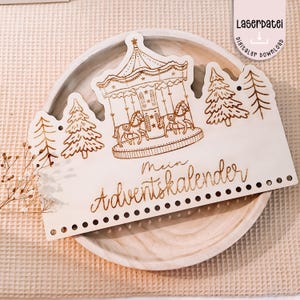 Puede incluir: Un calendario de adviento de madera cortado con láser con un diseño de carrusel. El carrusel presenta caballos y está rodeado de árboles. El texto "Mein Adventskalender" está escrito en una fuente decorativa. La imagen también incluye el texto "Laserdatei digitaler download".