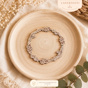 May include: A laser-cut wooden wreath with a floral design, featuring leaves and berries. The wreath is placed on a light-colored wooden plate. The image includes the text "LASERDATEI DIGITALER DOWNLOAD" and "INKLUSIVE KOMMERZIELLER NUTZUNG".