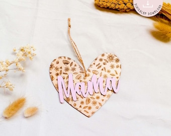 May include: A wooden heart-shaped ornament with a floral pattern and the word "Mama" in pink lettering. The ornament has a string attached for hanging.