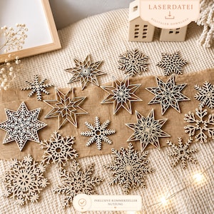 Puede incluir: Una colección de adornos de copos de nieve de madera en varios tamaños y diseños. Los copos de nieve cortados con láser están dispuestos sobre una superficie de tonos neutros, algunos con intrincados patrones de estrellas. El texto "LASERDATEI DIGITALER DOWNLOAD" y "INKLUSIVE KOMMERZIELLER NUTZUNG" es visible.