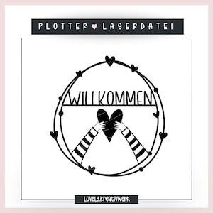 May include: Black and white design of a heart held by two hands with the word "Willkommen" above it. The design is surrounded by a circle of hearts.