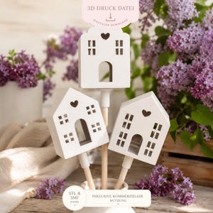 May include: Three white house-shaped ornaments with heart cutouts and window details. The houses are mounted on wooden sticks and arranged in a white vase. The image includes text that says "3D DRUCK DATEI" and "DIGITALER DOWNLOAD".