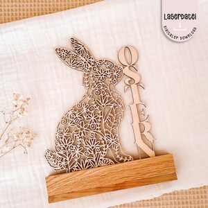Puede incluir: Decoración de conejo de Pascua de madera con diseño floral, sobre una base de madera. La palabra "OSTER" se muestra verticalmente junto al conejo. La imagen también incluye el texto "Laserdatei digitaler download".