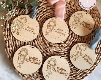 Puede incluir: Seis adornos circulares de madera con diseños cortados con láser. Los diseños incluyen niños que sostienen útiles escolares y el texto "endlich Schulkind" y "Mein 1. Schultag".