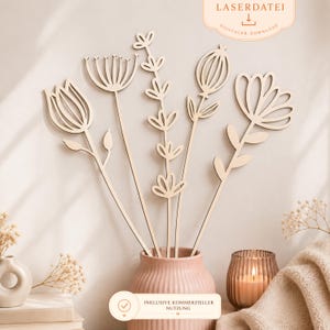 Op de afbeelding: Een verzameling houten bloemenuitsparingen in verschillende vormen, waaronder tulpen en andere gestileerde bloemen. De uitsparingen worden in een roze vaas getoond. De afbeelding bevat ook een kaars in een glazen houder en een beige deken.