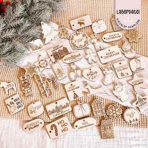 Könnte beinhalten: Eine Sammlung lasergeschnittener Weihnachtsornamente aus Holz in verschiedenen Formen, darunter Sterne, Schneeflocken und Geschenkboxen. Viele Ornamente zeigen festliche Texte wie "Merry Christmas" und "Winter". Die Ornamente sind hellbraun mit geätzten Designs.