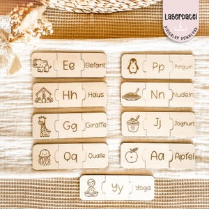 May include: Wooden alphabet puzzle pieces with engraved illustrations and words. Includes an elephant, penguin, house, noodles, giraffe, yogurt, jellyfish, apple, and yoga. The text "Laserdatei digitaler download" is in the upper right corner.