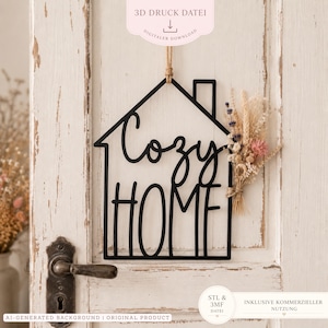 以下が含まれることがあります： 手書き風とブロック体のフォントで「Cozy HOME」と書かれた、黒い家型の壁掛けサイン。ジュート麻紐のループで吊り下げられており、ラベンダーや小麦の穂を含む小さなドライフラワーの束で装飾されています。