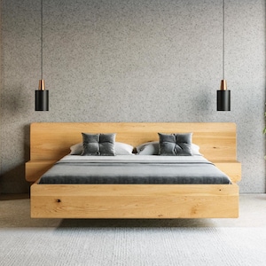 Könnte beinhalten: Ein helles Holzbettgestell mit integriertem Kopfteil und zwei angebrachten Nachttischen. Das Bett ist mit einer glatten grauen Bettdecke und zwei passenden quadratischen grauen Zierkissen bezogen. Die Struktur weist ein klares Design auf.