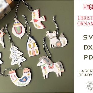 Może przedstawiać: Zestaw 9 laserowo wyciętych ozdób choinkowych w różnych wzorach inspirowanych stylem skandynawskim, w tym renifer, dom, drzewo, lis, ptak, królik i koń. Ozdoby są białe z kolorowymi detalami i gotowe do dekoracji.