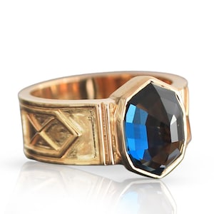 May include: A gold ring with a blue gemstone set in a hexagonal bezel. The band features a geometric design.