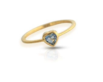 May include: A gold ring with a heart-shaped, light blue gemstone. The ring is set on a thin, gold band. The gemstone is a light blue color. The ring is displayed on a white background. The text "GemsRainbowCo" is at the bottom.