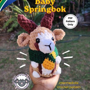 May include: A crochet plush toy of a baby springbok with tan, white, and dark brown yarn, featuring dark brown horns, a green scarf, and a yellow accent. The image includes text reading Baby Springbok, PDF Pattern Only, and Intermediate crochet pattern.